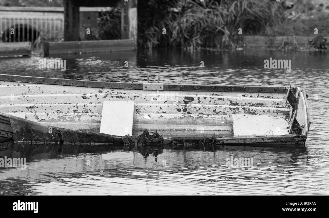 Kleines Holzboot in einem See und zur Hälfte unter Wasser verlassen. Schwarz und weiß. Stockfoto