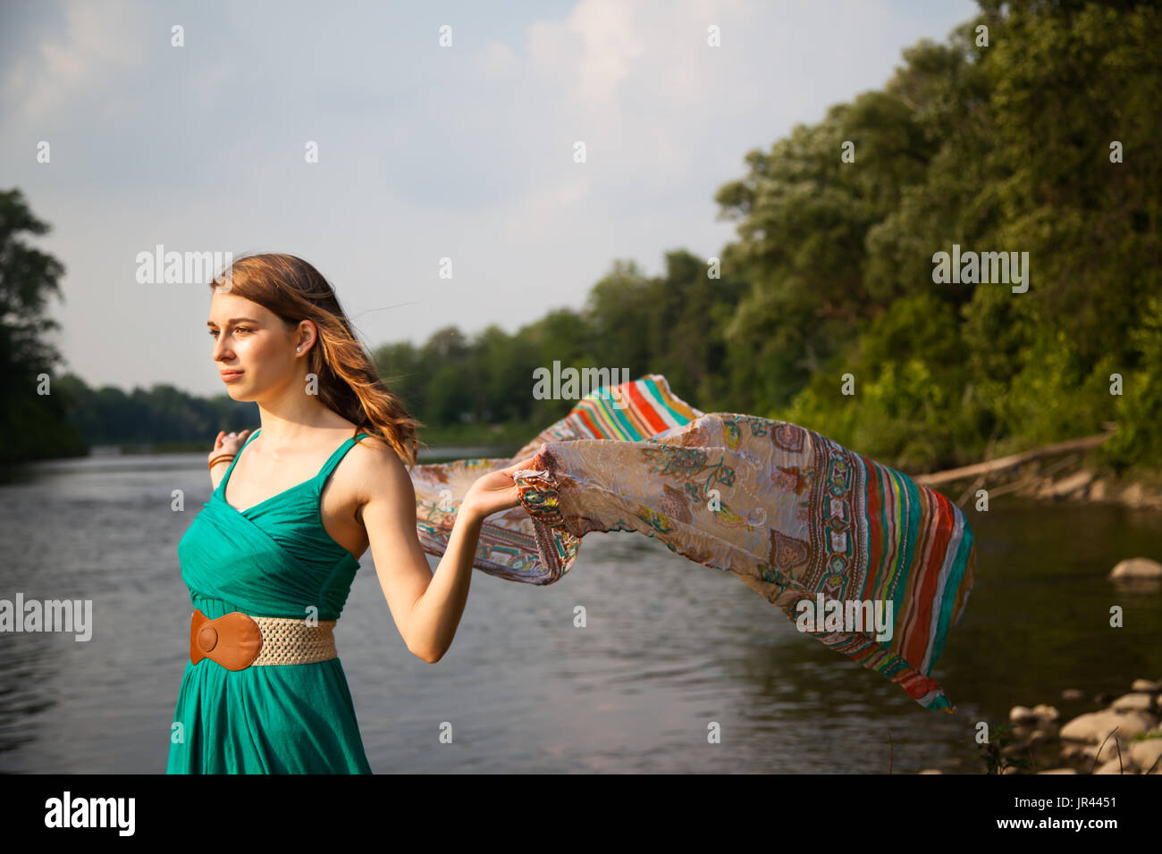 Junge Frau mit einem blaugrün Kleid steht an einem Fluss / See holding im Wind flatternden Teal trendigen Schal.   Sie ist entspannt und ruhig während Gefühl t Stockfoto