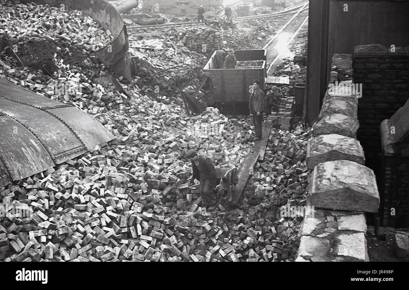 1940 s, historischen, Bild zeigt die große Ziegel und Mauerwerk nach dem Abriss der Öfen und die Gebäude der berühmten Dowlais Eisenhütte am Hang mit Blick auf Merthyr Tydfil, Wales, UK Links, und Arbeitnehmer, die sie in Bewegung durch Schubkarren. Stockfoto
