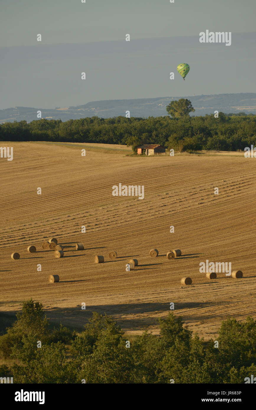 Hochformat von Heuballen auf einem Feld mit grünen Ballon steigen im Hintergrund. Ende der Sonne werfen lange Schatten über die Landschaft. Royal, Frankreich. Stockfoto