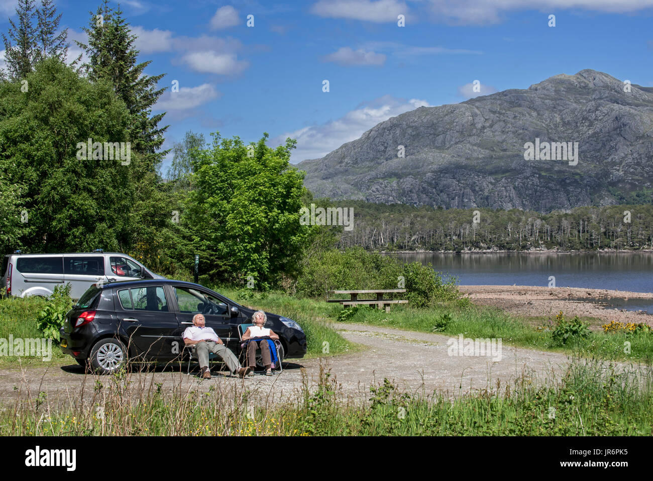 Älteres Ehepaar Sonnenbaden am Picknickplatz am Ufer des Loch Maree, Wester Ross, Schottisches Hochland, Schottland Stockfoto