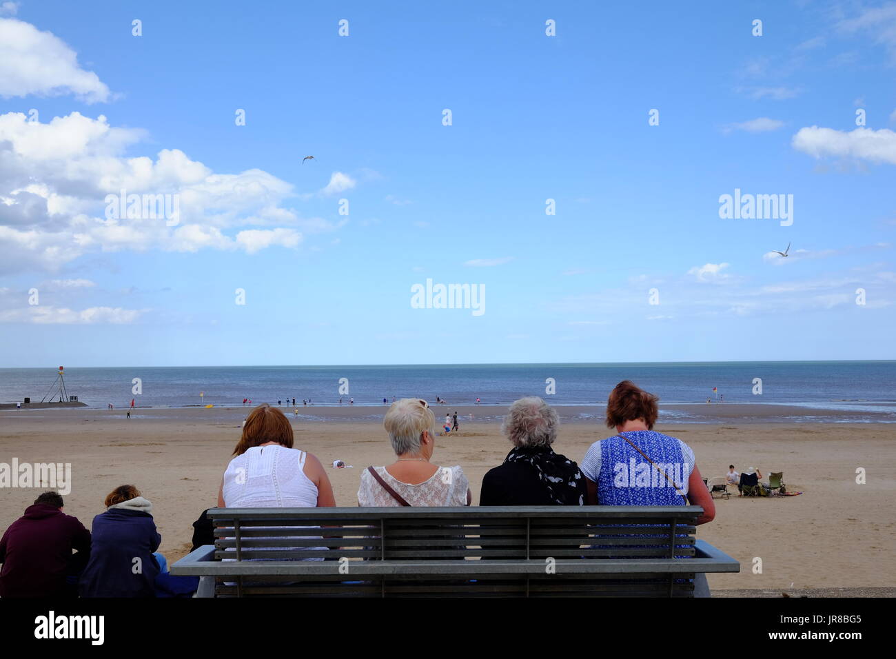 Vier Damen halten, um auf einer Bank an der Strandpromenade am Mablethorpe in Lincolnshire auf ihre Sommerferien zu entspannen. Stockfoto