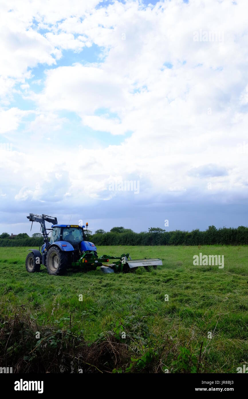 Ein Traktor mäht Rasen auf einer Farm in Lincolnshire, bleibt der Rasen um Heu zu machen. Stockfoto