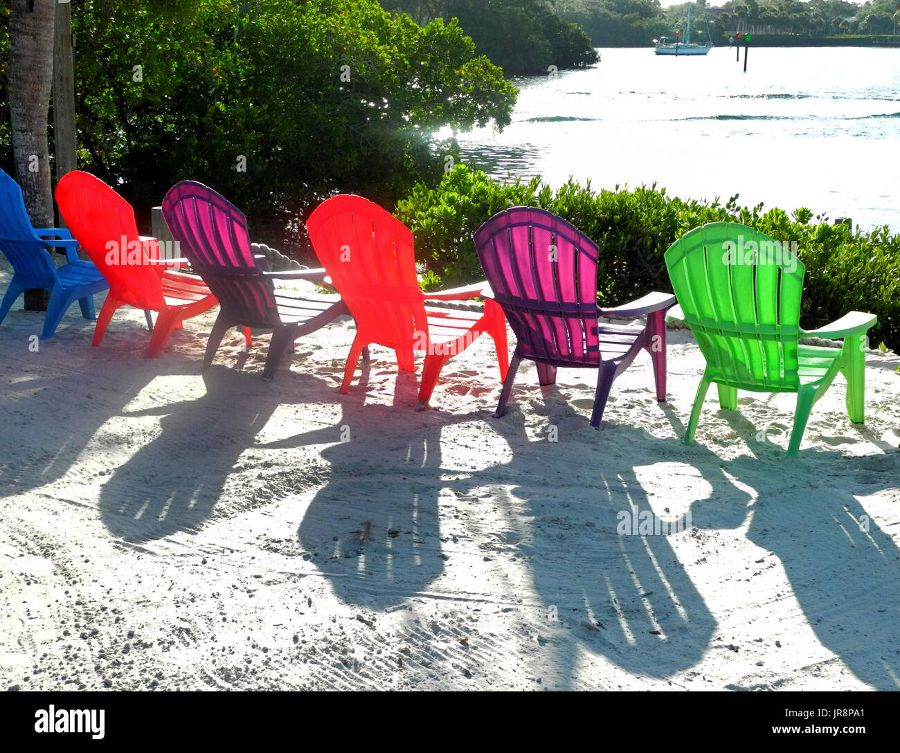 Bunte transluzente Kunststoff Liegestühle laden Entspannung und erstellen Schatten aus strahlendem Sonnenschein auf einer sandigen Uferpromenade entlang dem Gulf Intracoastal Waterway in Sarasota County, Florida, USA. Stockfoto