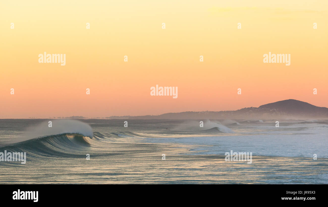 Brechende Welle bei Sonnenaufgang am Sunshine Beach, mit Mount Coolum im Hintergrund Stockfoto