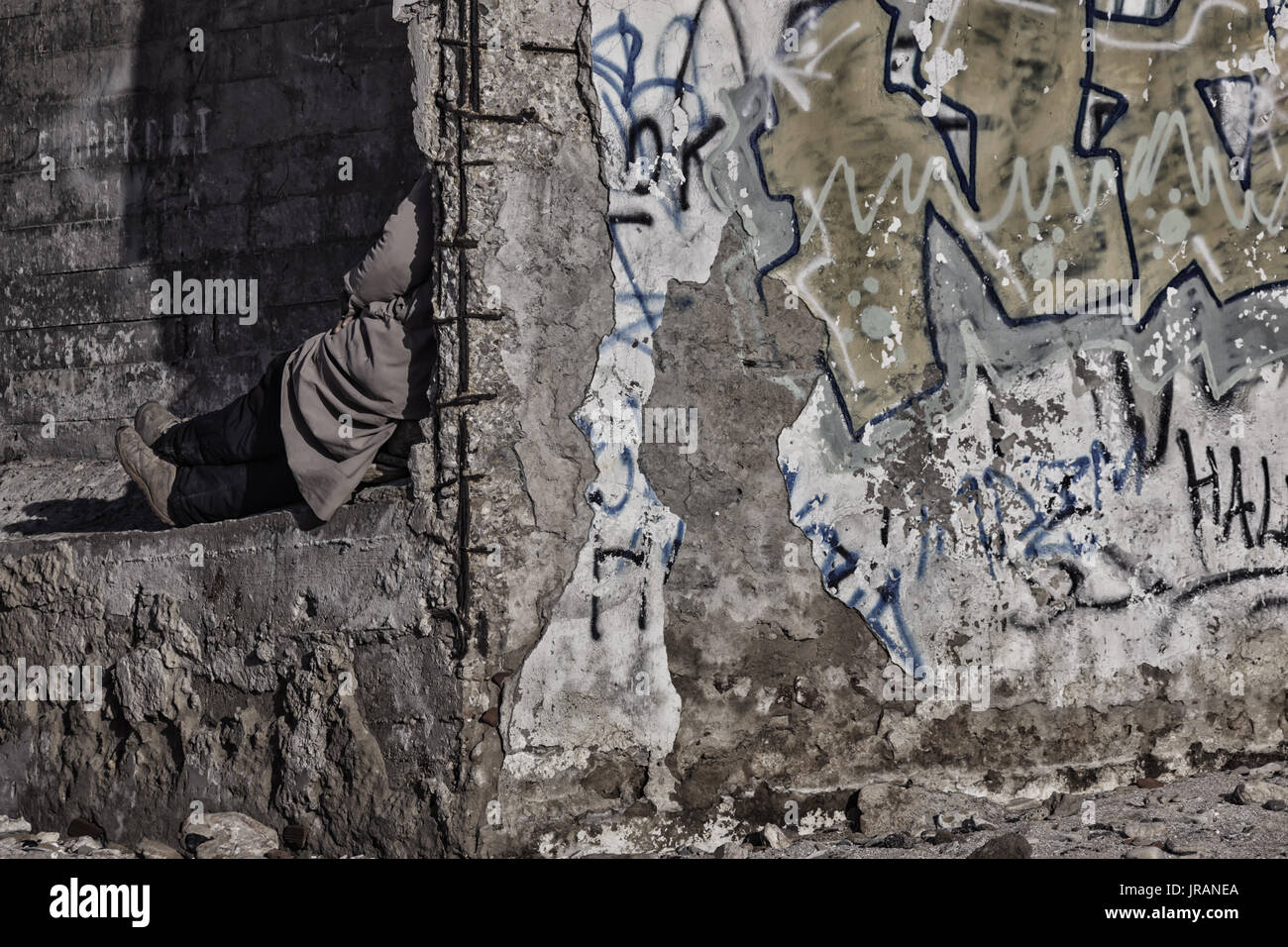Ein Obdachloser Mann oder eine Frau sitzt hinter einer Mauer außerhalb eines alten Gebäude aus Stein. Stockfoto