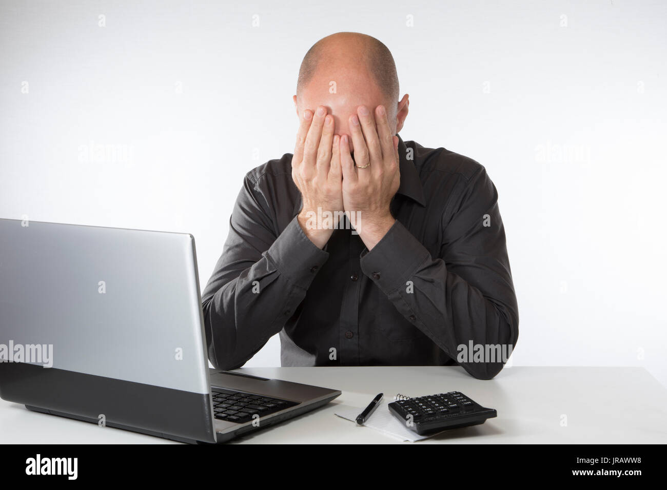 Verzweifelt, hoffnungslos Mann sitzt mit seinen Kopf in seine Hände, als er sitzt seine Konten tun an seinem Laptop. Stockfoto