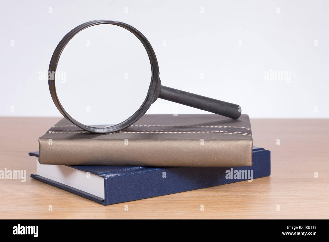 Zwei gebundene Bücher mit einer Lupe Balancieren auf der Kante auf der Oberseite mit Blick auf eine weiße Wand über einen Schreibtisch mit Kopie der Platz in einem konzeptionellen imag Stockfoto