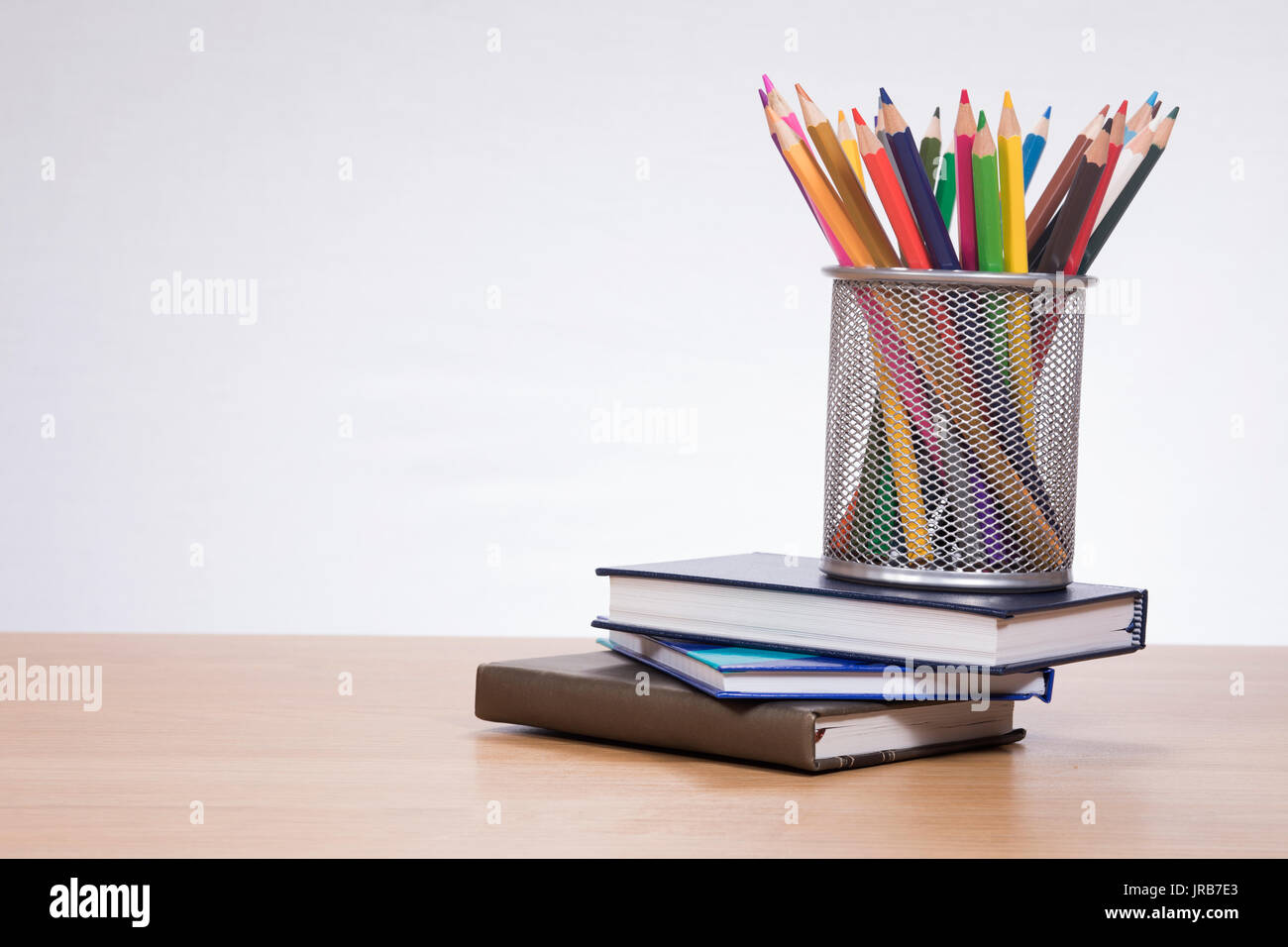 Halter mit Buntstiften auf Stapel Bücher gegen einfachen Hintergrund Stockfoto