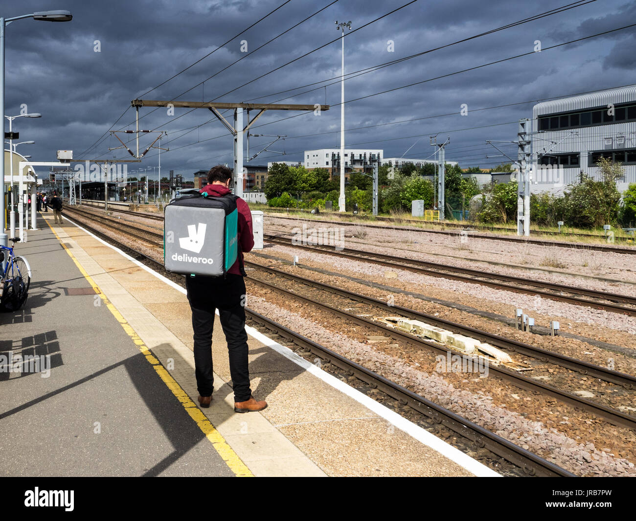 Mit dem Zug - eine Deliveroo Deliveroo fast food Kurier Fahrer wartet ein bummelzug in Cambridge, Großbritannien Stockfoto
