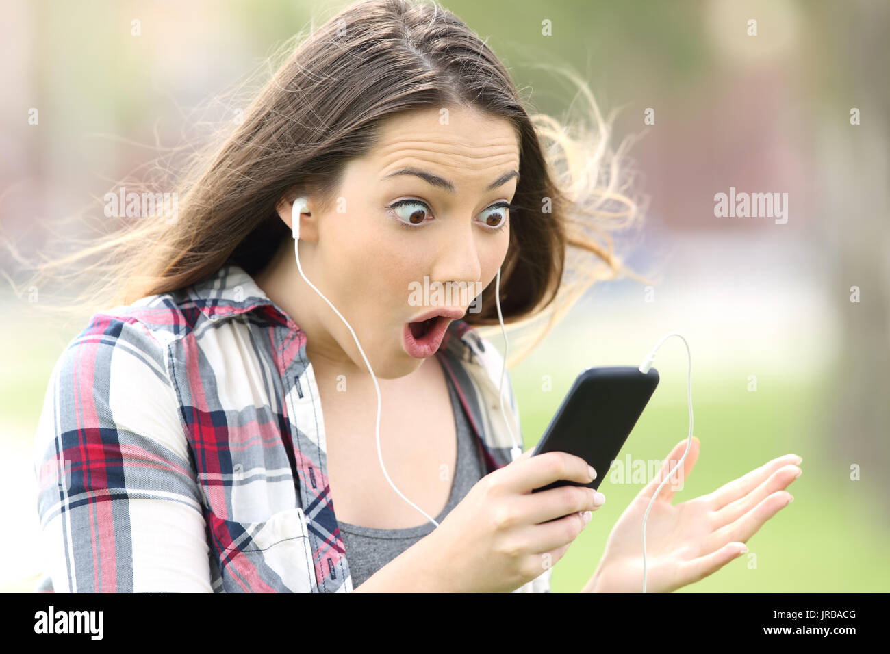 Erstaunt Mädchen auf Linie Musik zuhören und zuschauen Medieninhalte im Freien in einem park Stockfoto