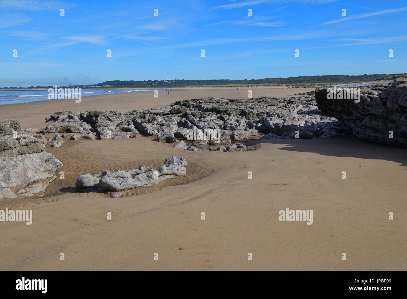 Ebbe auf ogmore Strand mit dem Dorf Newton im Hintergrund und ein paar Spaziergänger und ihre Hunde. Die niedrige tideleaves viel Rock Pools. Stockfoto