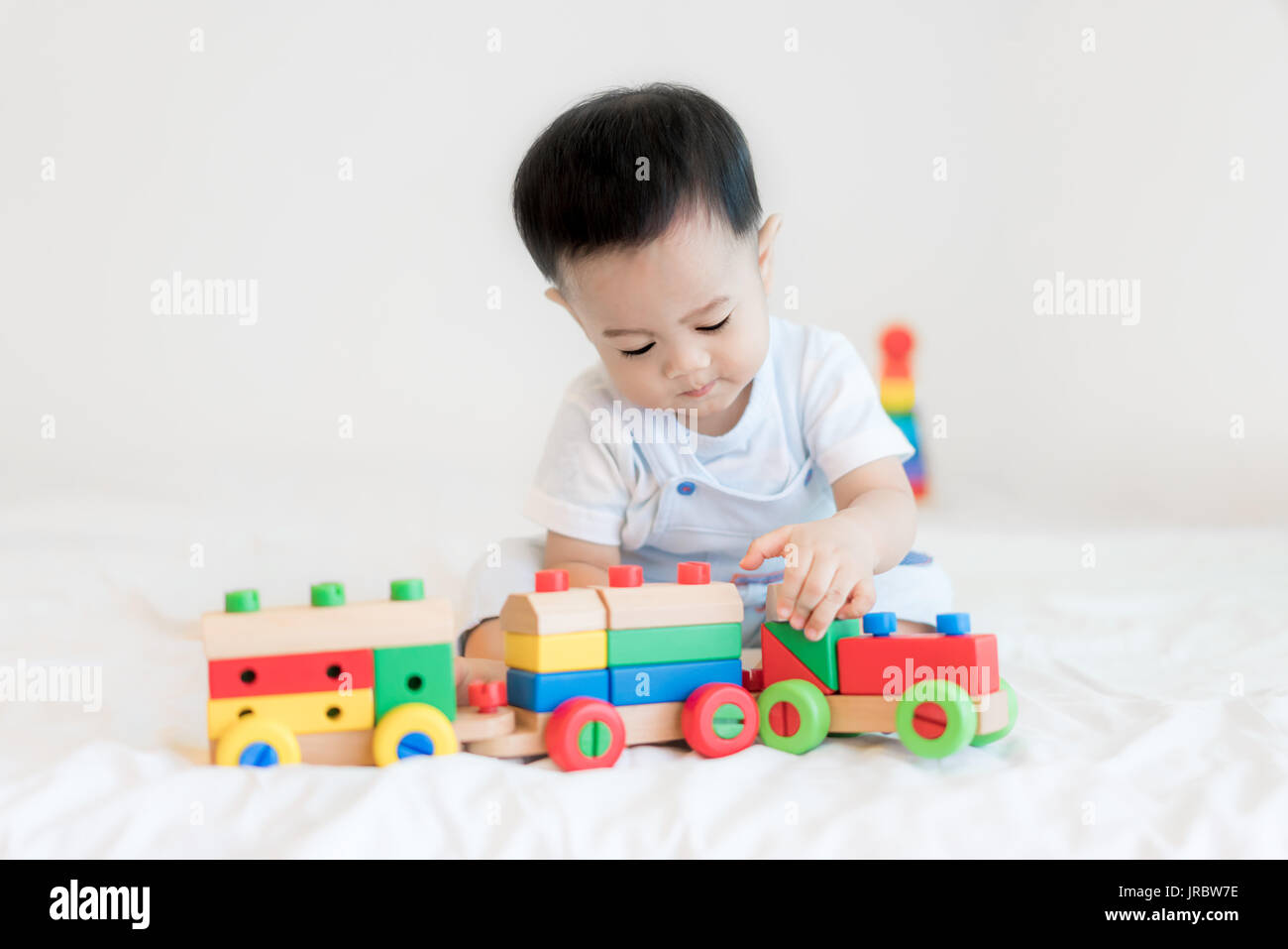 Entzückende asiatische Baby junge 9 Monate am Bett sitzen und spielen mit Farbe Holzeisenbahn Spielzeug zu Hause. Stockfoto