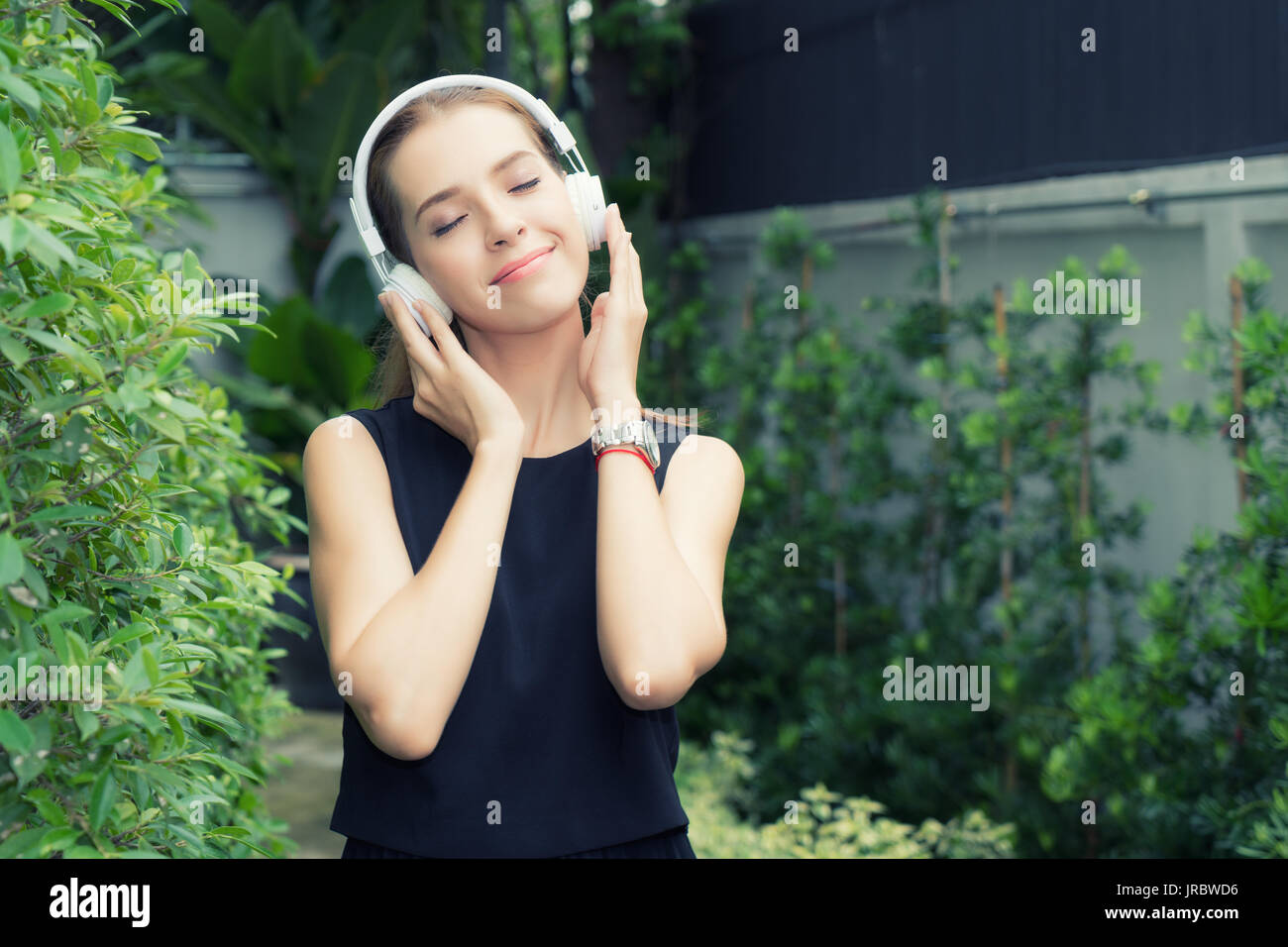Schöne Russische Frau Musik hören, während Sie die Augen schließen, mit weißen Kopfhörer im Garten zu Hause. Entspannend. Stockfoto