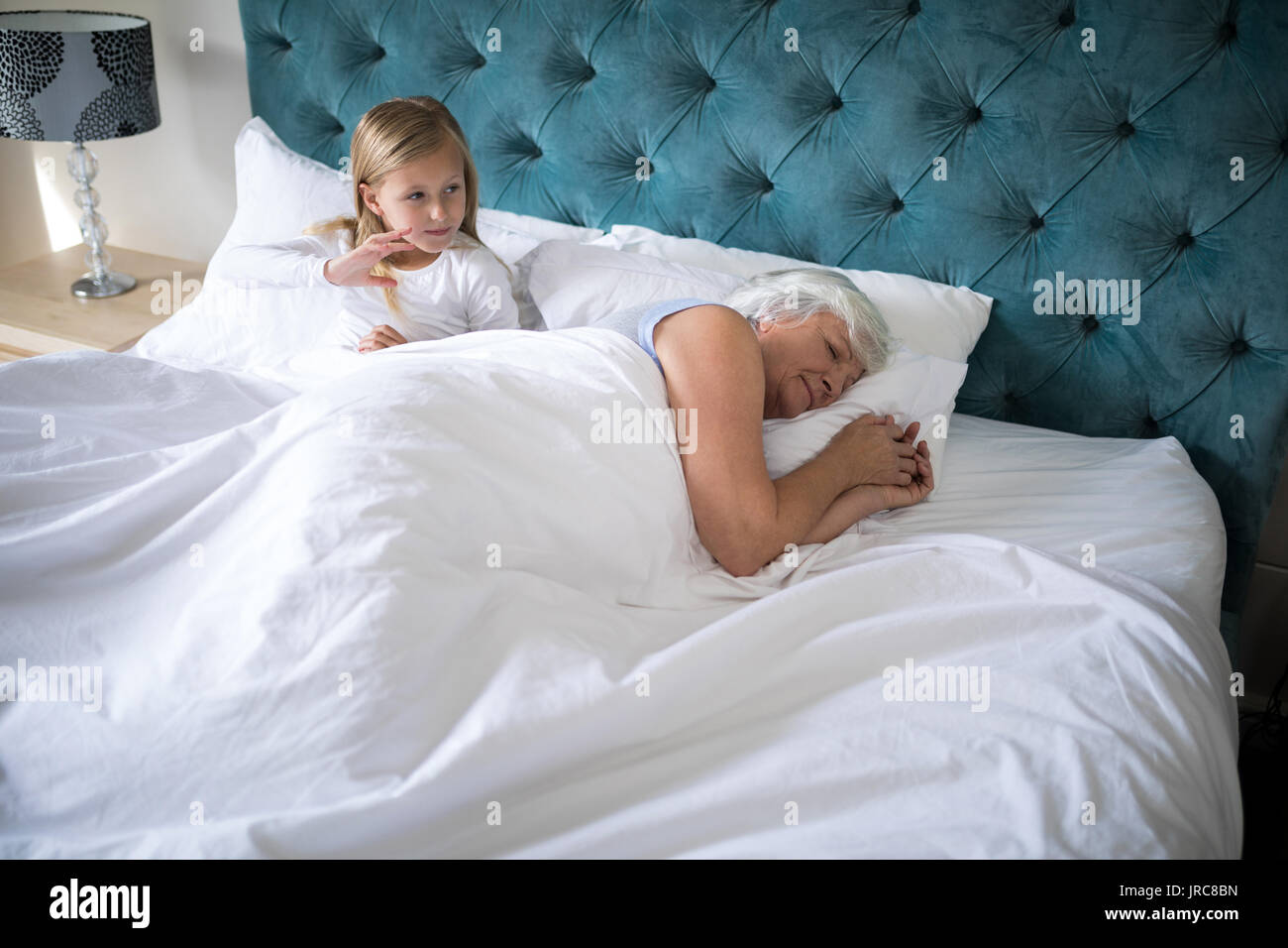Großmutter schlafen auf Bett, während Mädchen hinter ihr im Schlafzimmer  sitzen Stockfotografie - Alamy