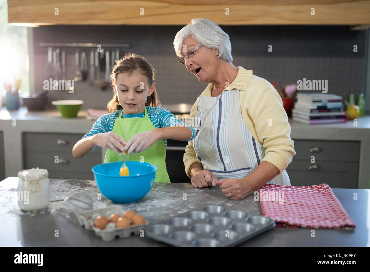 Enkelin Aufschlagen der Eier und Großmutter aufpassen beim Stehen in der Küche Stockfoto