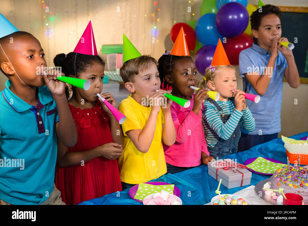 Verspielte Kinder blasen party Hörner im Stehen durch die Tabelle während der Geburtstagsfeier Stockfoto