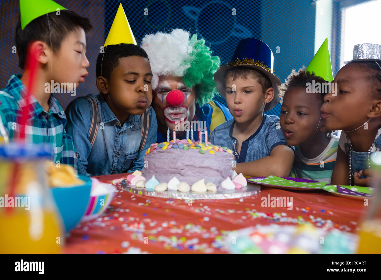 Kinder mit clown bläst Kerzen auf Kuchen während Geburtstag Stockfoto