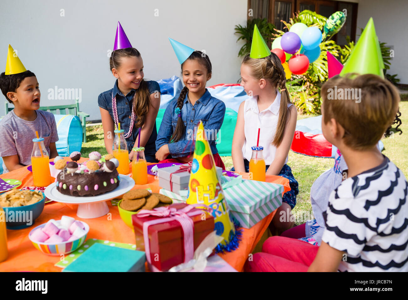 Glückliche Kinder sprechen, beim Sitzen am Tisch während der Geburtstagsfeier im Hof Stockfoto