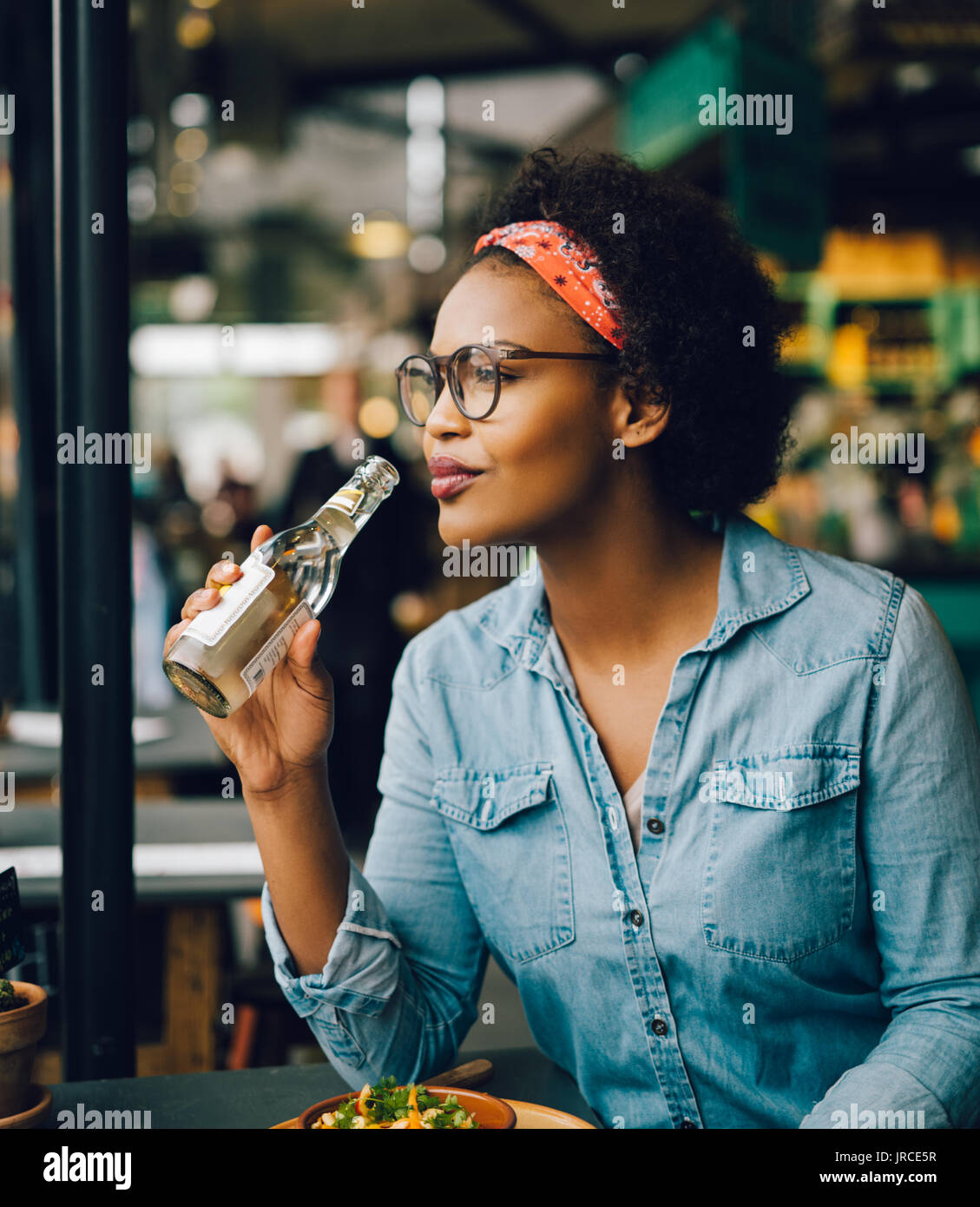 Inhalt junge Frau lächelnd und mit Blick durch ein Fenster beim Trinken ein Getränk und Essen allein in einem Bistro Stockfoto