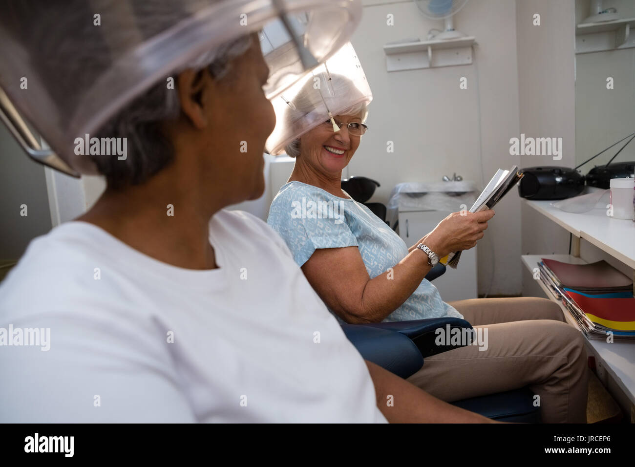 Weibliche Freunde sich einander, während unter Haar Dampfgarer im Salon sitzen Stockfoto