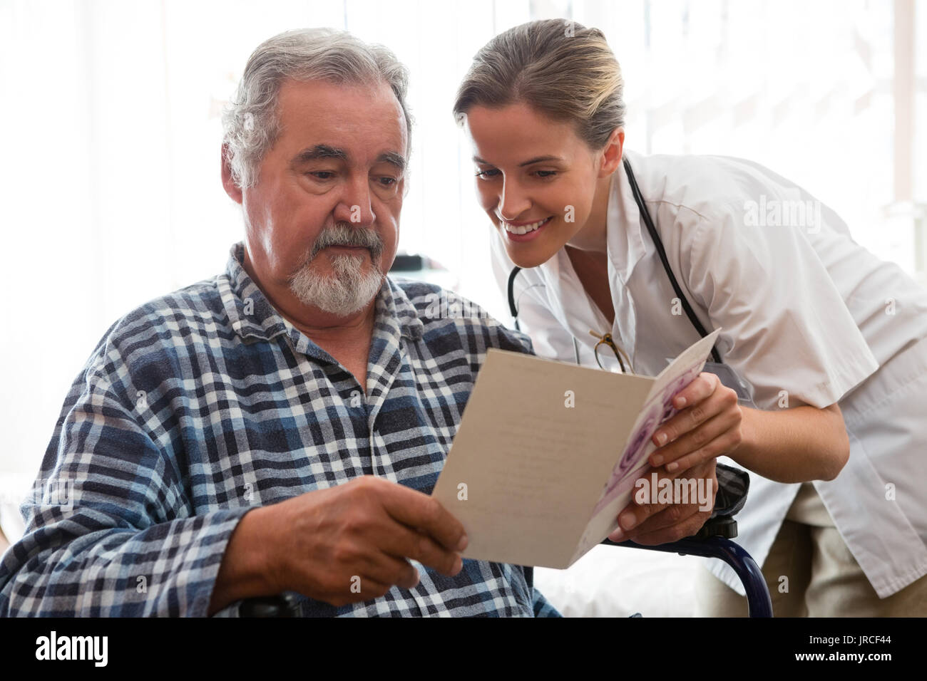 Ärztin mit Grußkarte an Patienten sitzen auf Rollstuhlfahrer im Pflegeheim Stockfoto