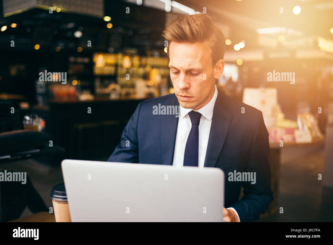 Junge Geschäftsmann im Anzug alleine sitzen an einem Tisch in einem Café einen Kaffee trinken und online arbeiten mit einem Laptop Stockfoto