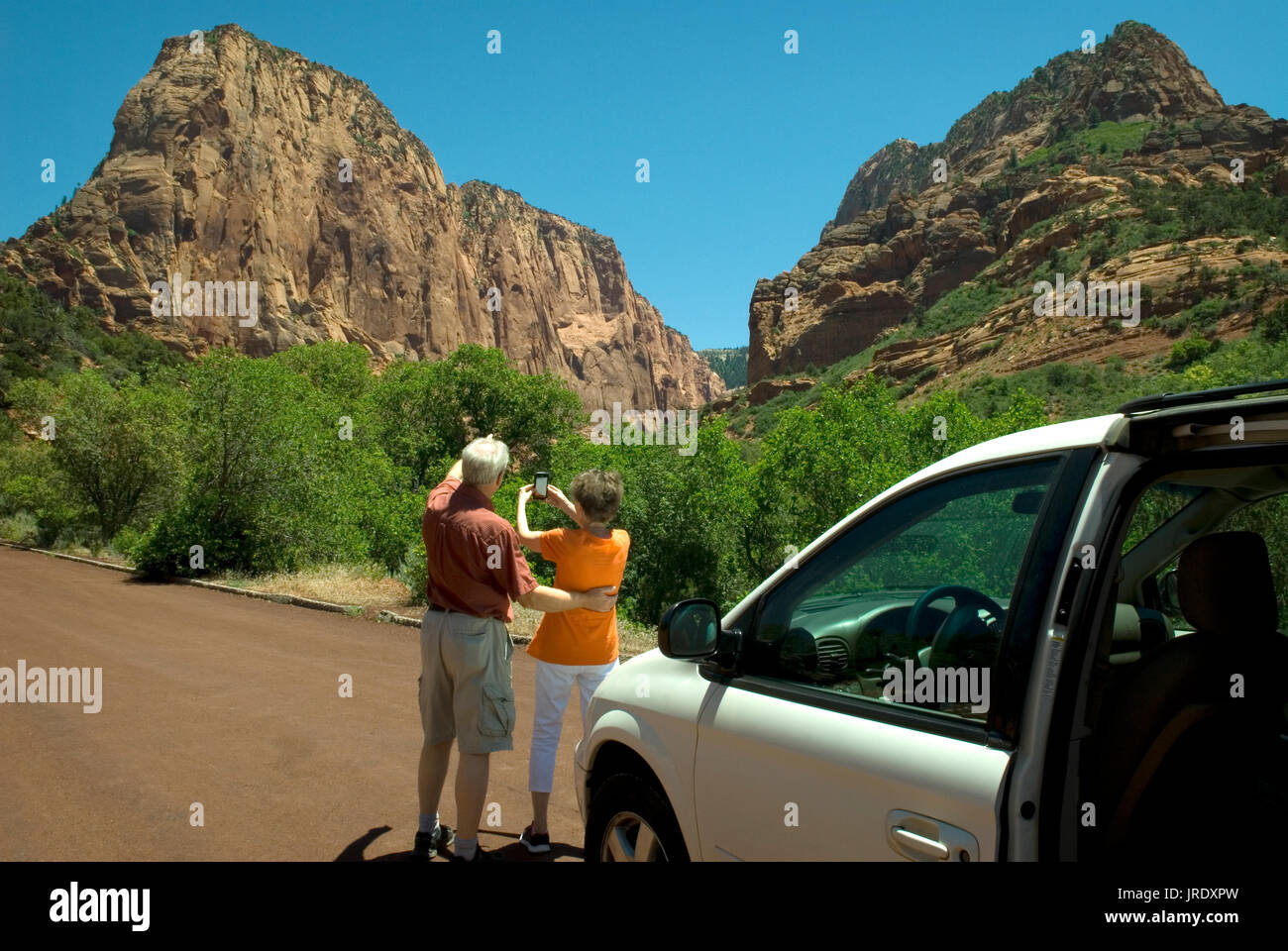 Kaukasisches Seniorenpaar (60-70) in den Kolob Canyons im Zion National Park Utah USA. Frau trägt orangenes Hemd und fotografiert, während der Mann zeigt. Stockfoto