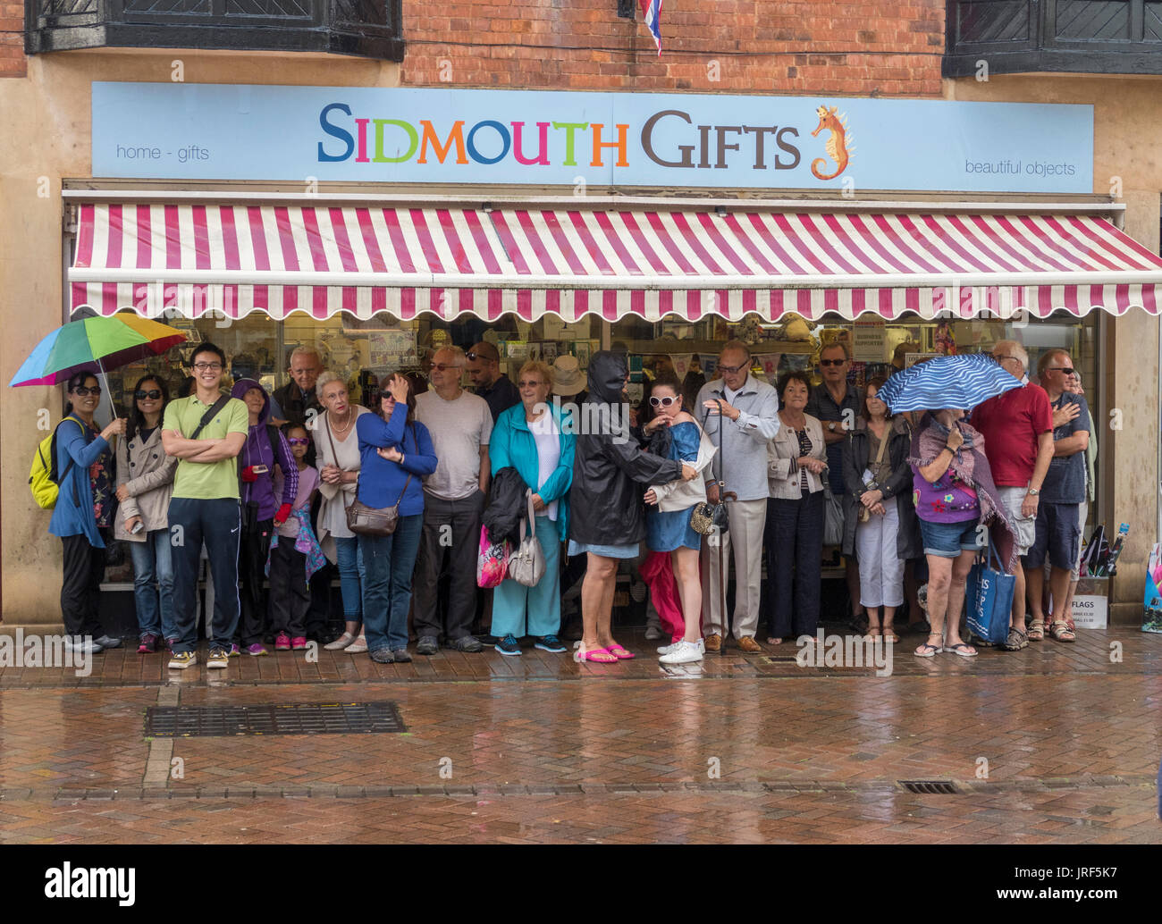 Eine Masse von Menschen drängen sich zusammen und Schutz vor dem Regen unter einem Shop Markise in Honiton, Devon. Stockfoto
