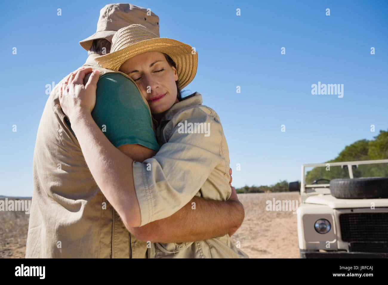 Paar umarmt von Off Road Fahrzeug auf Feld während der sonnigen Tag Stockfoto