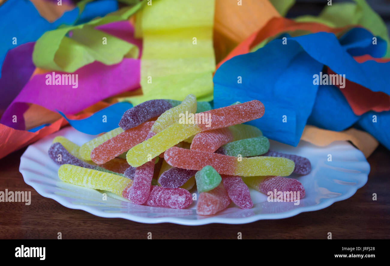 Saurer Wurm süß Süßwaren behandelt auf weiße Platte mit Party Luftschlangen im Hintergrund Stockfoto