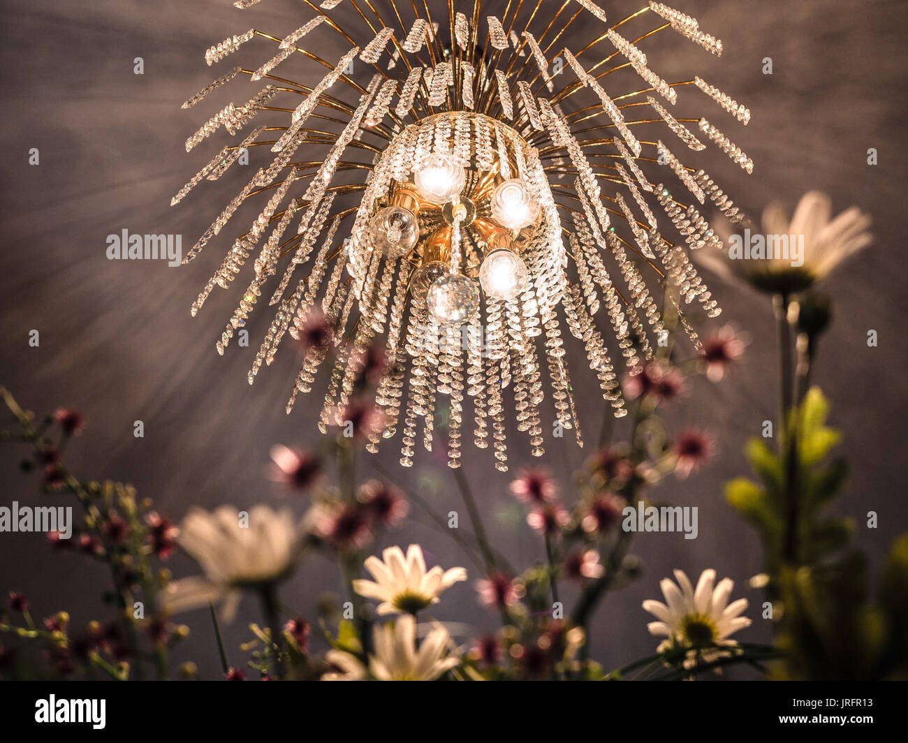 Kronleuchter aus Kristall mit goldenem Licht und künstliche Blumen. Stockfoto