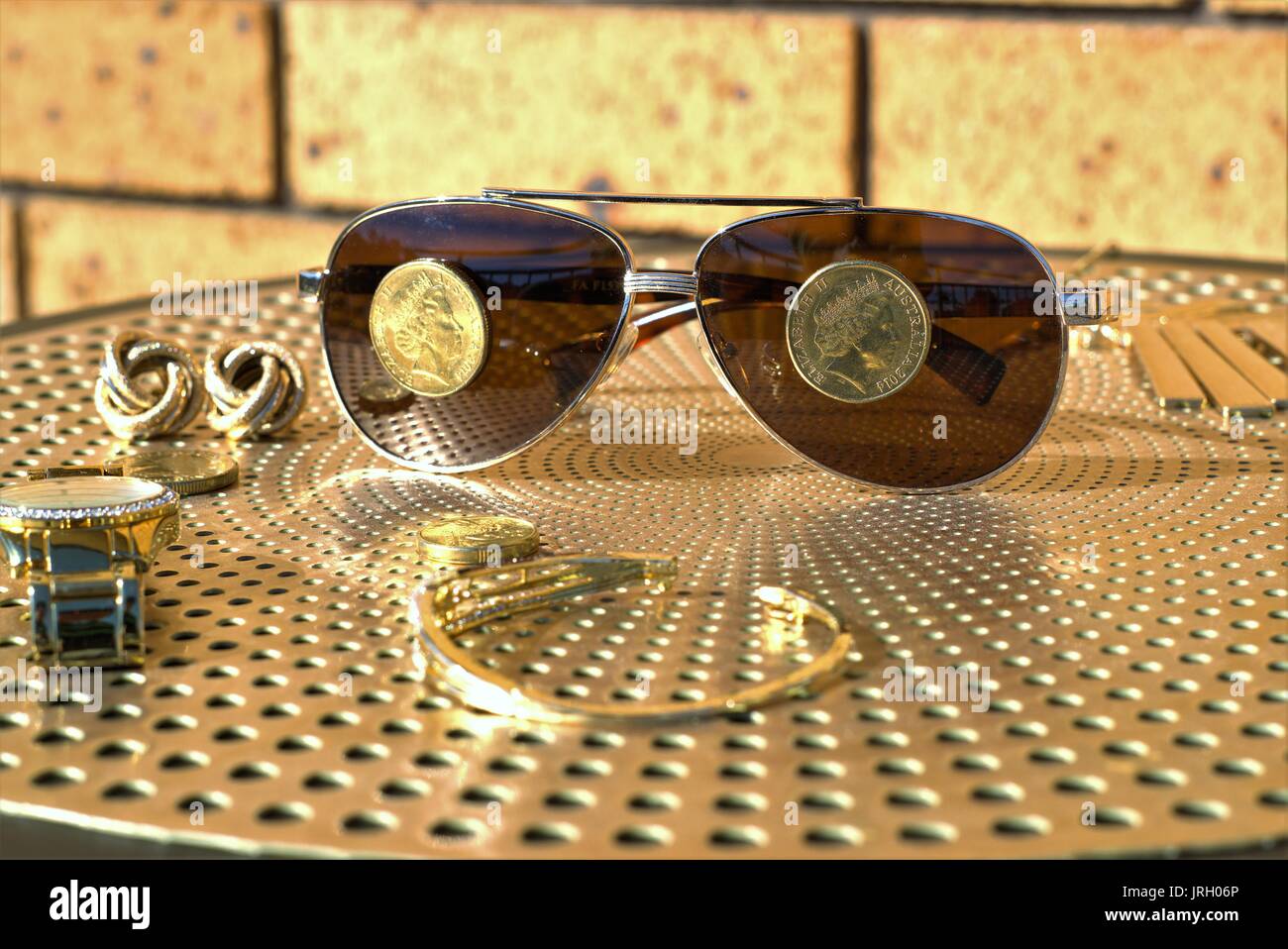 Australische Münzen auf eine Sonnenbrille. Australische 1 Dollar Münzen auf Sonnenbrillen, Gold Diamond Watch und anderen Gold Schmuck auf Tisch Stockfoto