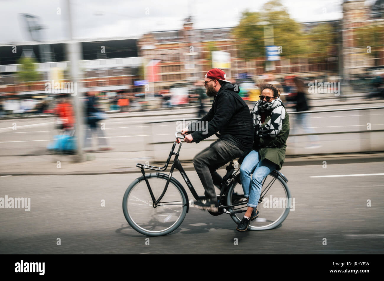 Amsterdam, Niederlande - 27 April 2017: ein Mann Radfahrer trägt eine junge Frau als Beifahrer auf dem Fahrrad, Reiten durch die Straße von Amsterdam, Niederlande Stockfoto