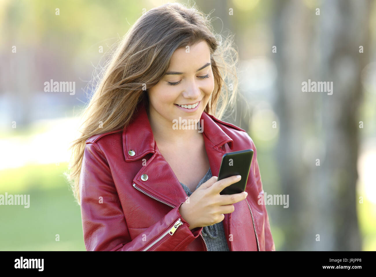 Mode teen das Tragen der roten Jacke Chatten in Einklang mit einem Mobiltelefon zu Fuß in einem Park Stockfoto