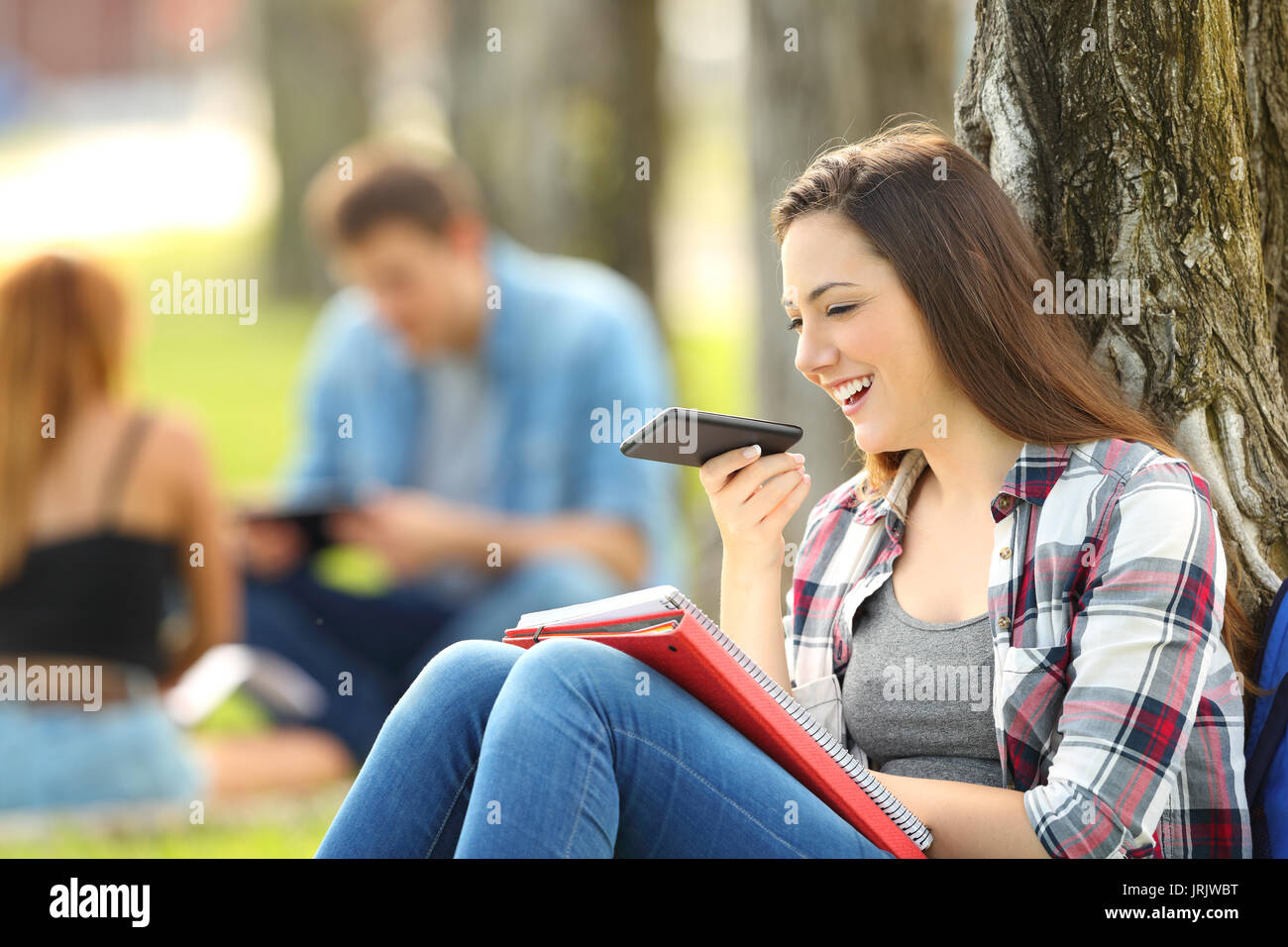 Schüler mithilfe der Spracherkennung mit einem Smartphone auf die Noten an, die auf dem Gras in einem Park aufzeichnen Stockfoto