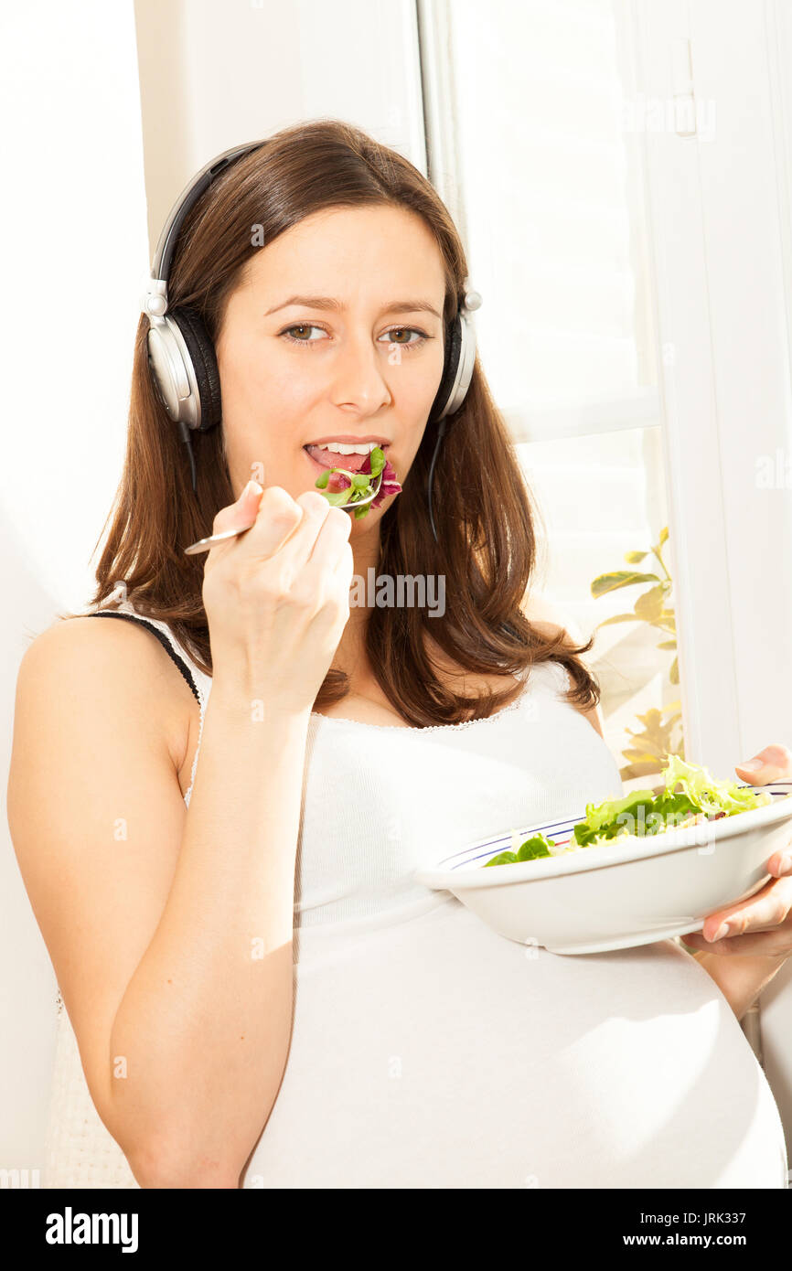 Schwangere Frau Salat essen und Musik hören Stockfoto