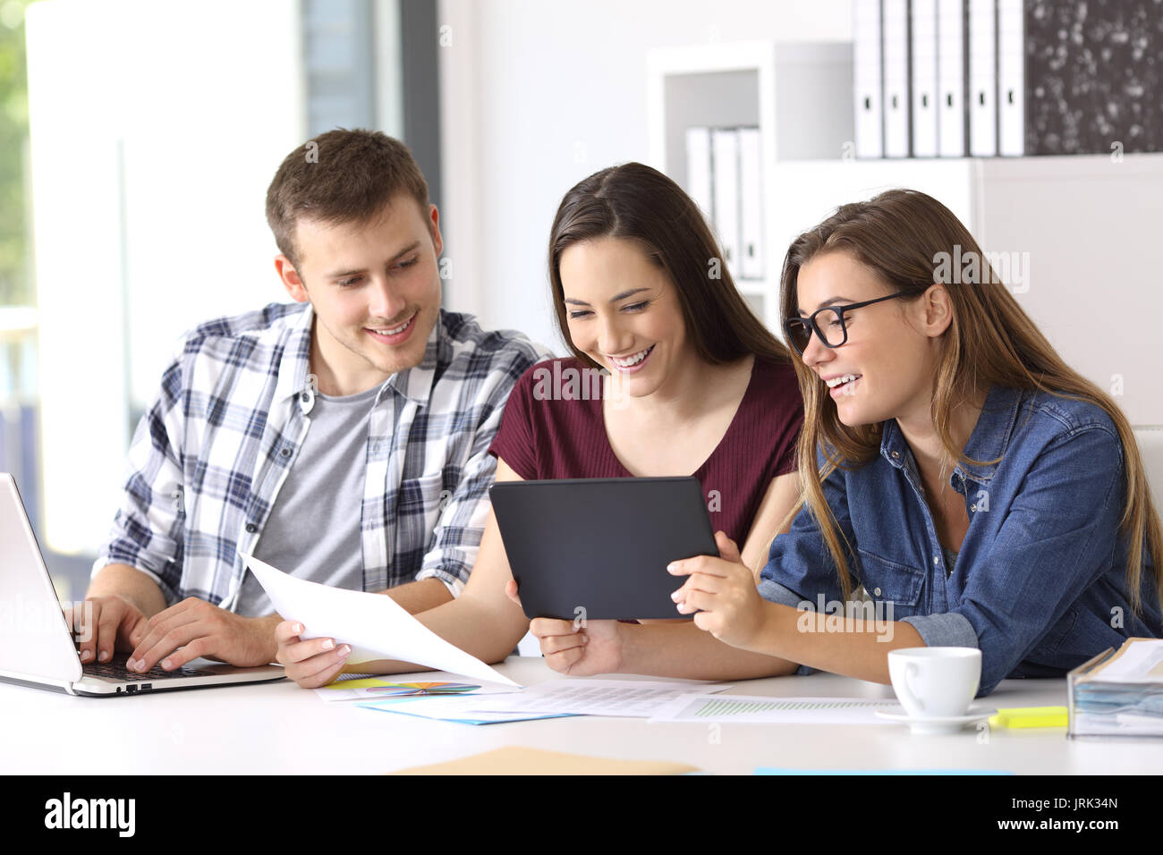 Drei glückliche Mitarbeiter arbeiten auf der Linie mit einer Tablette und Dokumente im Büro Stockfoto