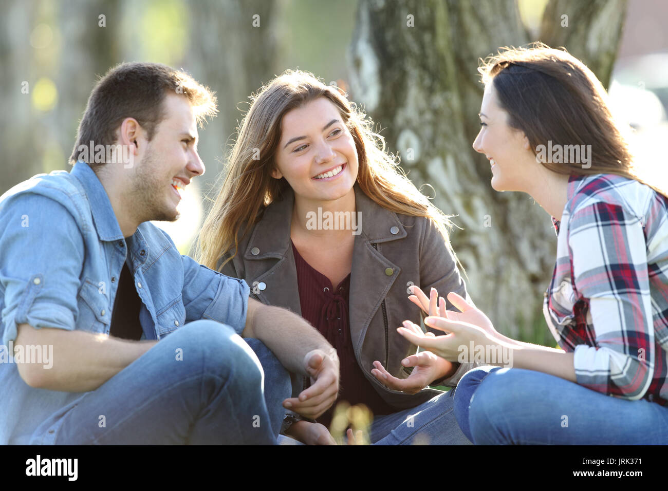 Drei glückliche Freunde sprechen, sitzen auf der Wiese im Park Stockfoto