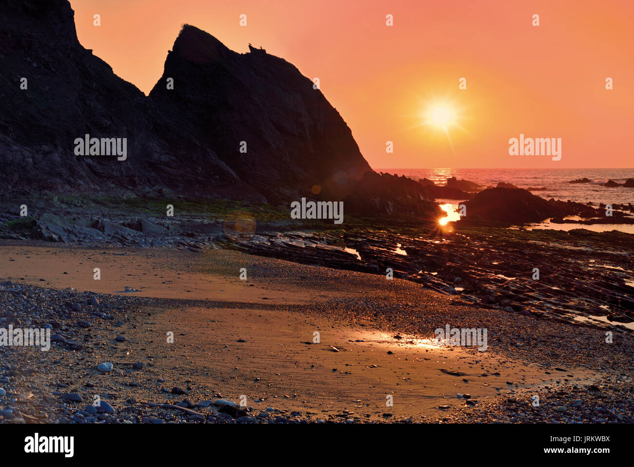 Romantischer Sonnenuntergang am wilden Strand mit riesigen Felsen Stockfoto