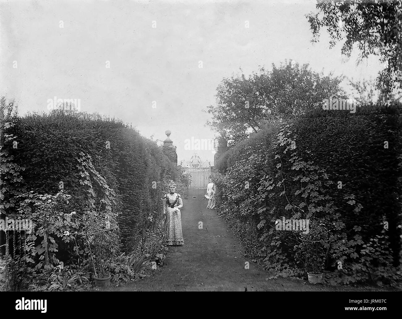 1890 Albumen Foto von einem formalen Garten mit Pfad zu der eisernen Tore und zwei Damen, die in der viktorianischen Mode der Zeit Stockfoto
