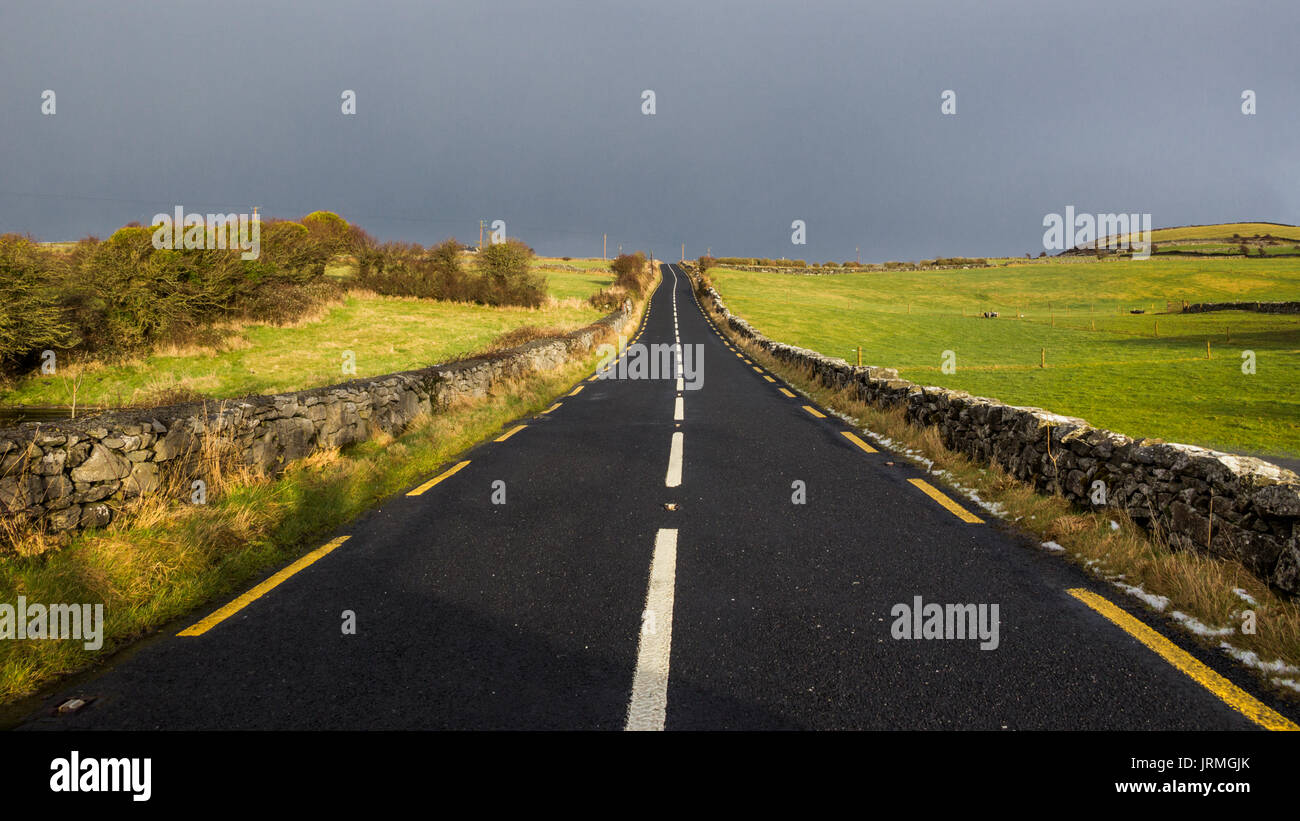 Straße durch das ländliche Irland mit einem düsteren Himmel. Stockfoto