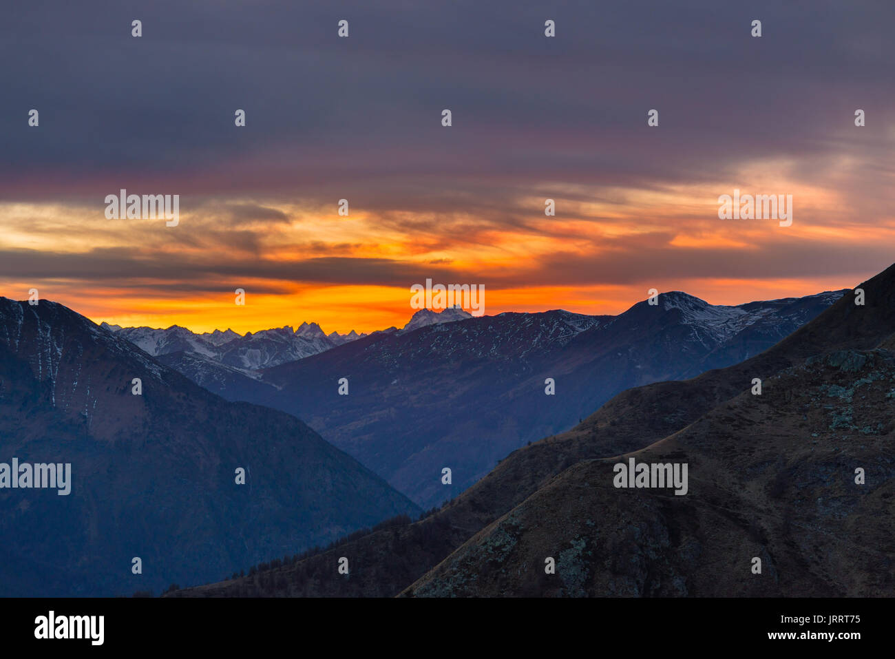 Bunte Sonnenlicht hinter majestätischen Berggipfeln der italienisch-französischen Alpen, von Ferne gesehen. Nebel und Dunst über die Täler, herbstliche Stockfoto