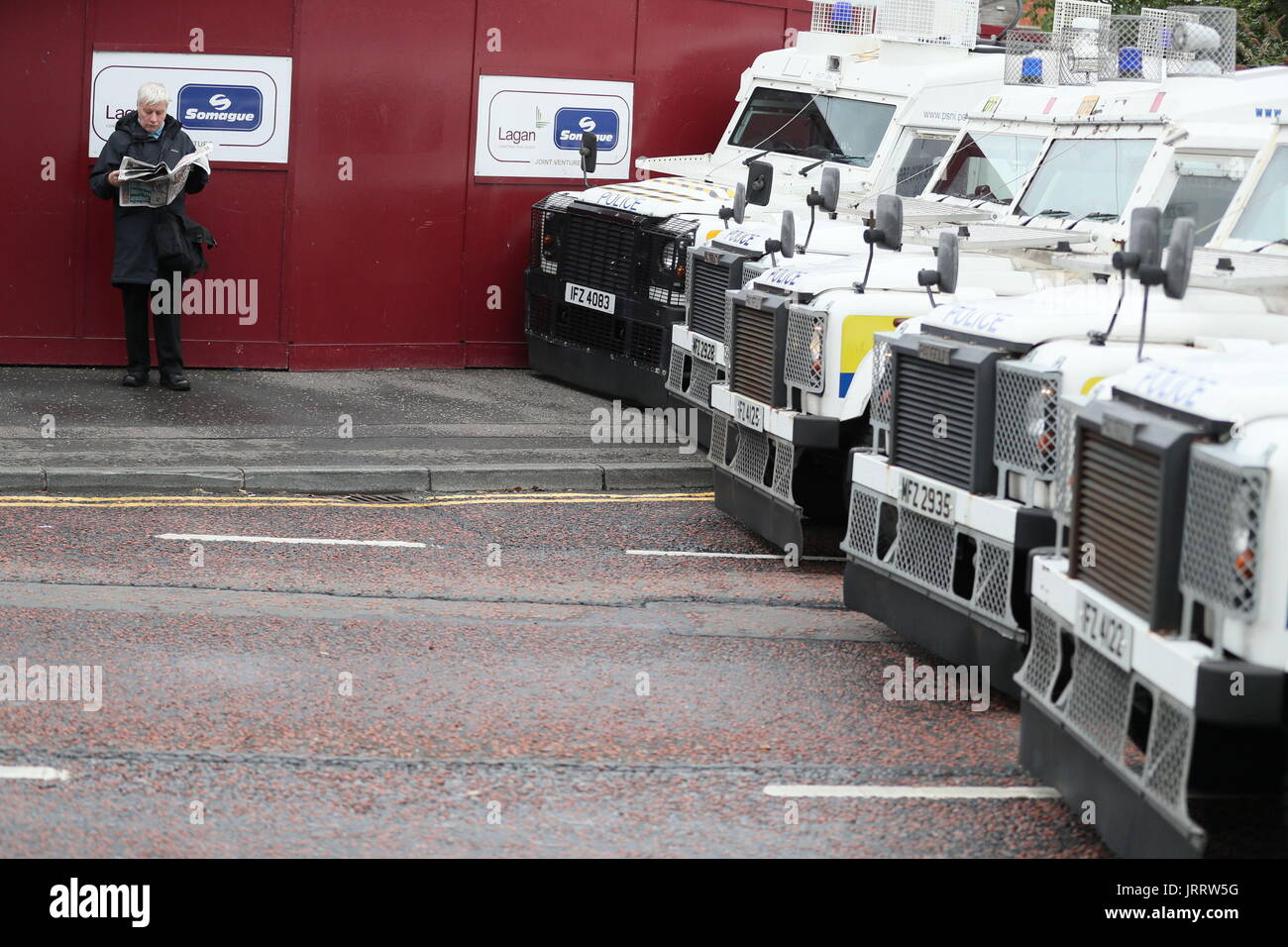 Ein Mann liest Zeitung, wie er auf eine Polizei-Barriere wartet, im Anschluss an eine Anti-Internierung-Parade in Belfast zu zerstreuen. Stockfoto