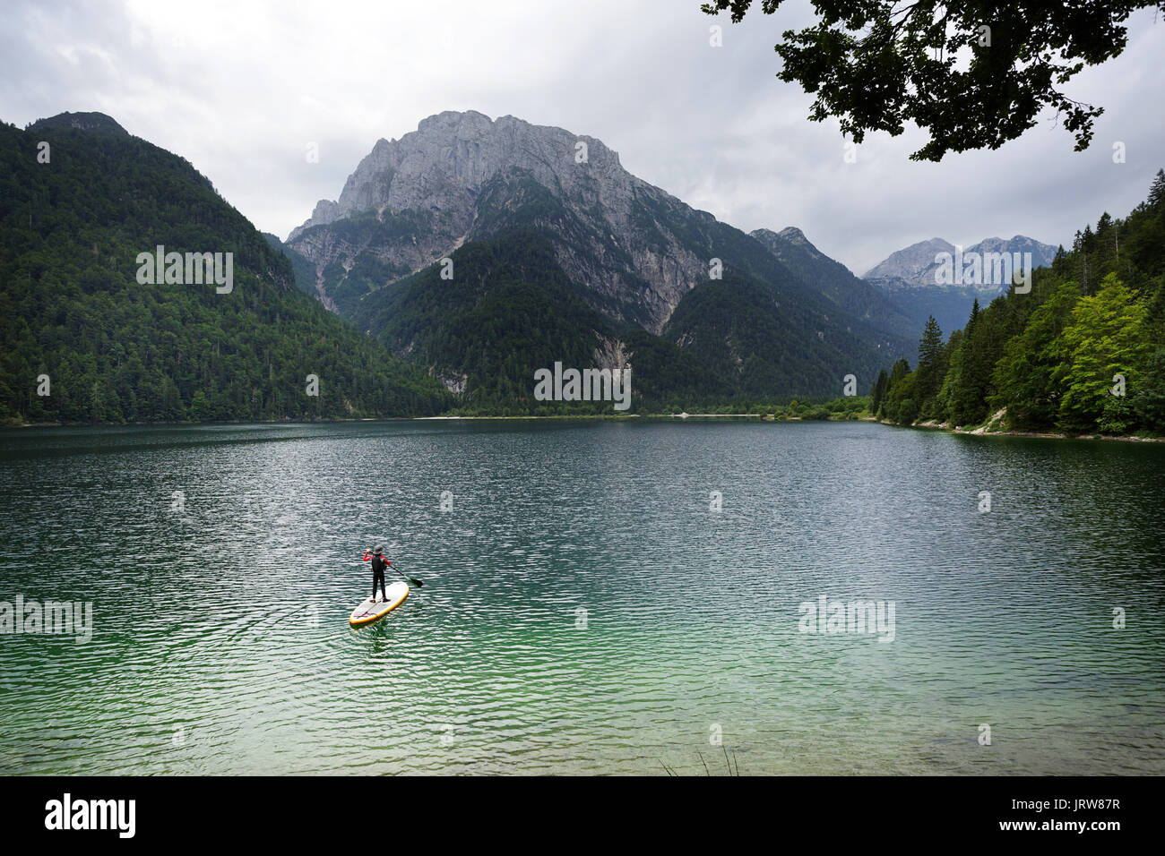 Junge in einem Neopren Dry Suit und ein Hut Stand Up Paddling am alpinen See Predil, Italien. Stockfoto