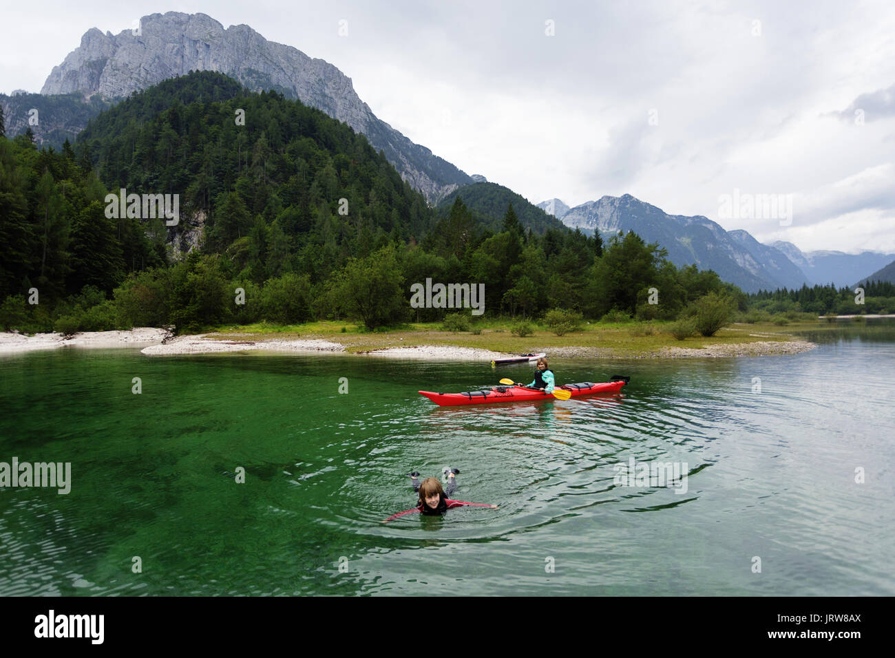 Mutter in Kajak ihr Sohn spielen in das smaragdgrüne Wasser auf alpinen See. Lago di Predil, Italien. Stockfoto