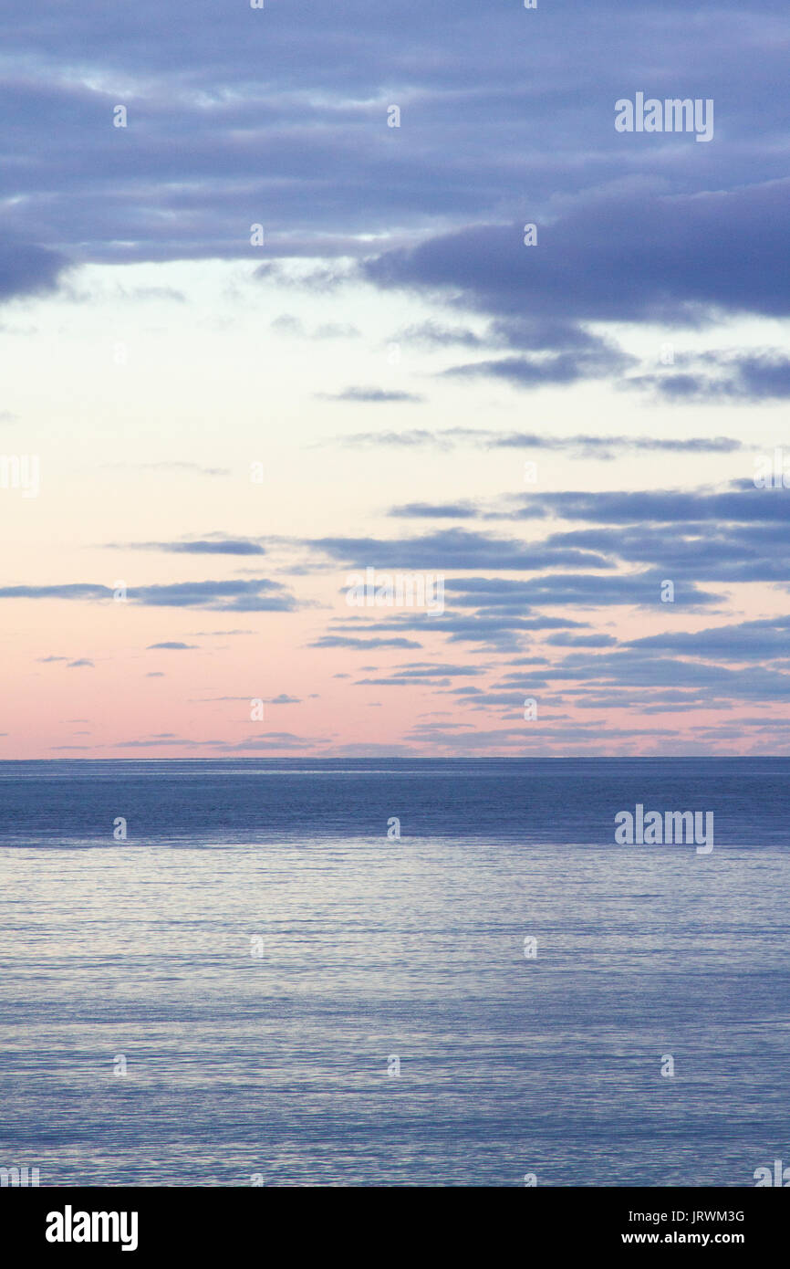 Ruhiger Blick auf das Meer bei Sonnenuntergang mit einem rosa Himmel und dunklen Gewitterwolken über dem Horizont Stockfoto