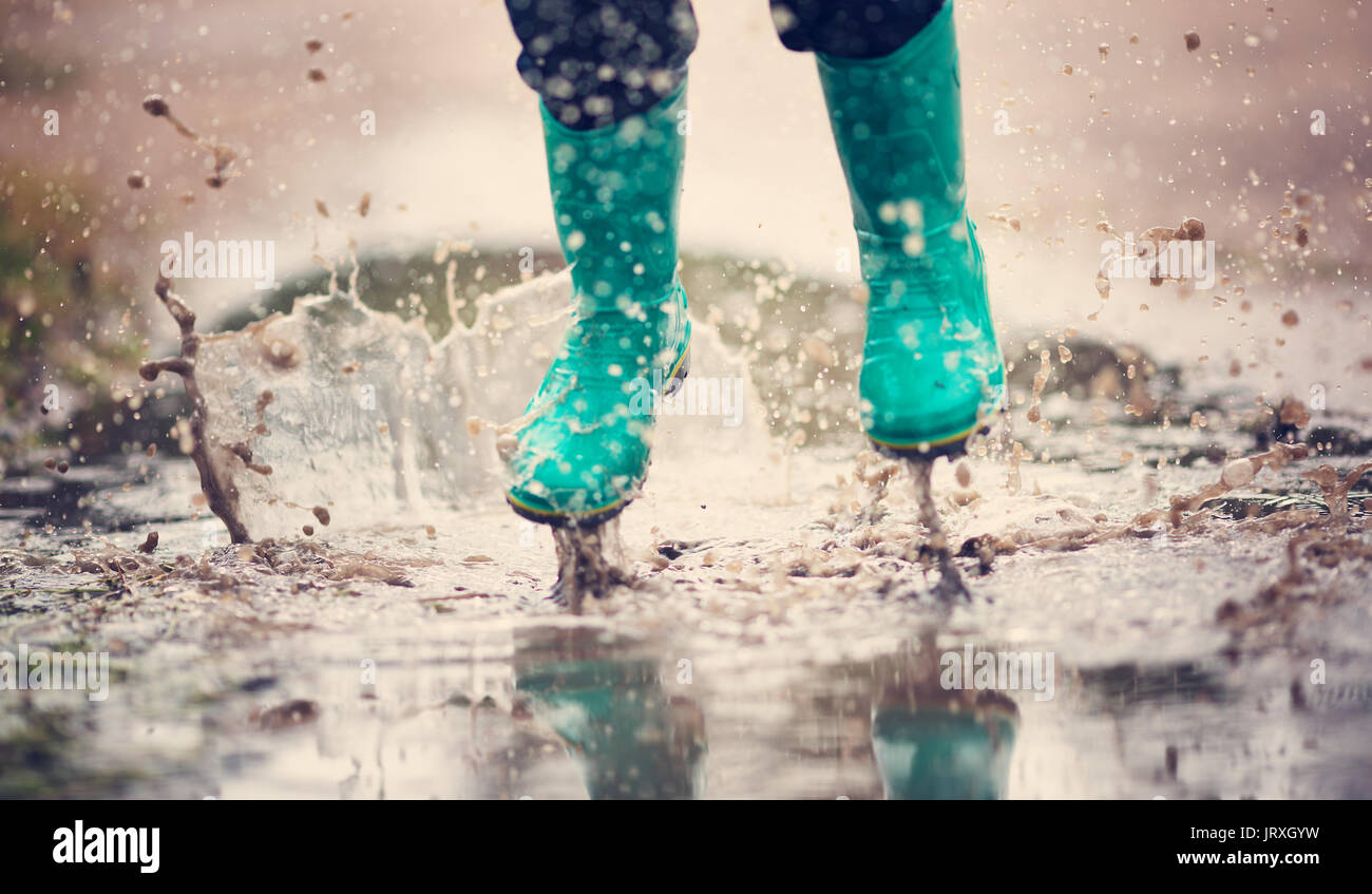 Kind wandern in Gummistiefel in der Pfütze auf Regenwetter. Junge unter