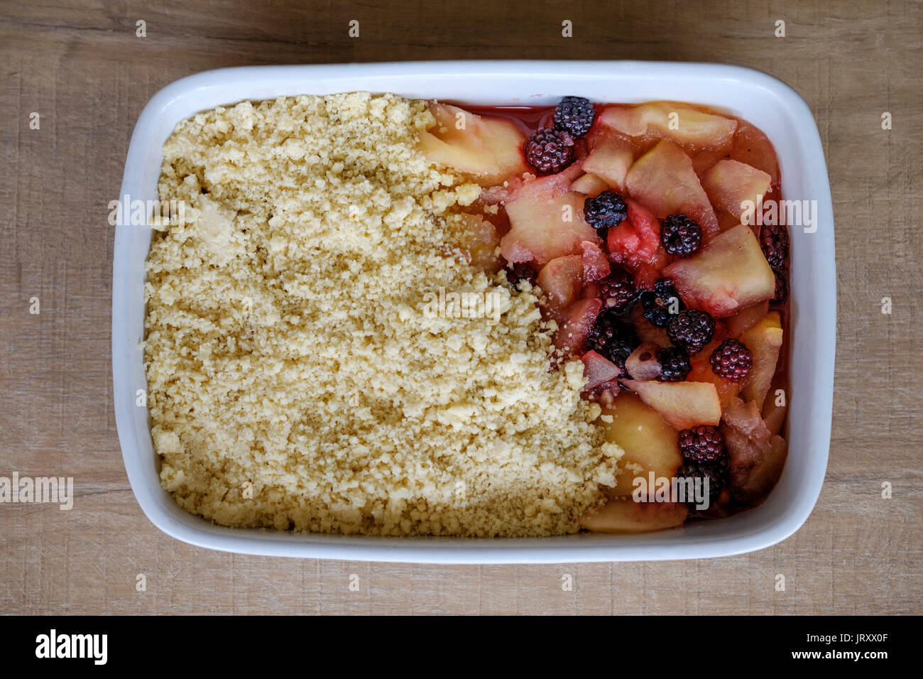 Ein teilweise hergestellter traditioneller englischer Apfel- und Brombeerkrümel. Der Kuchen befindet sich in einer großen Keramikbackform und kann gekocht werden Stockfoto