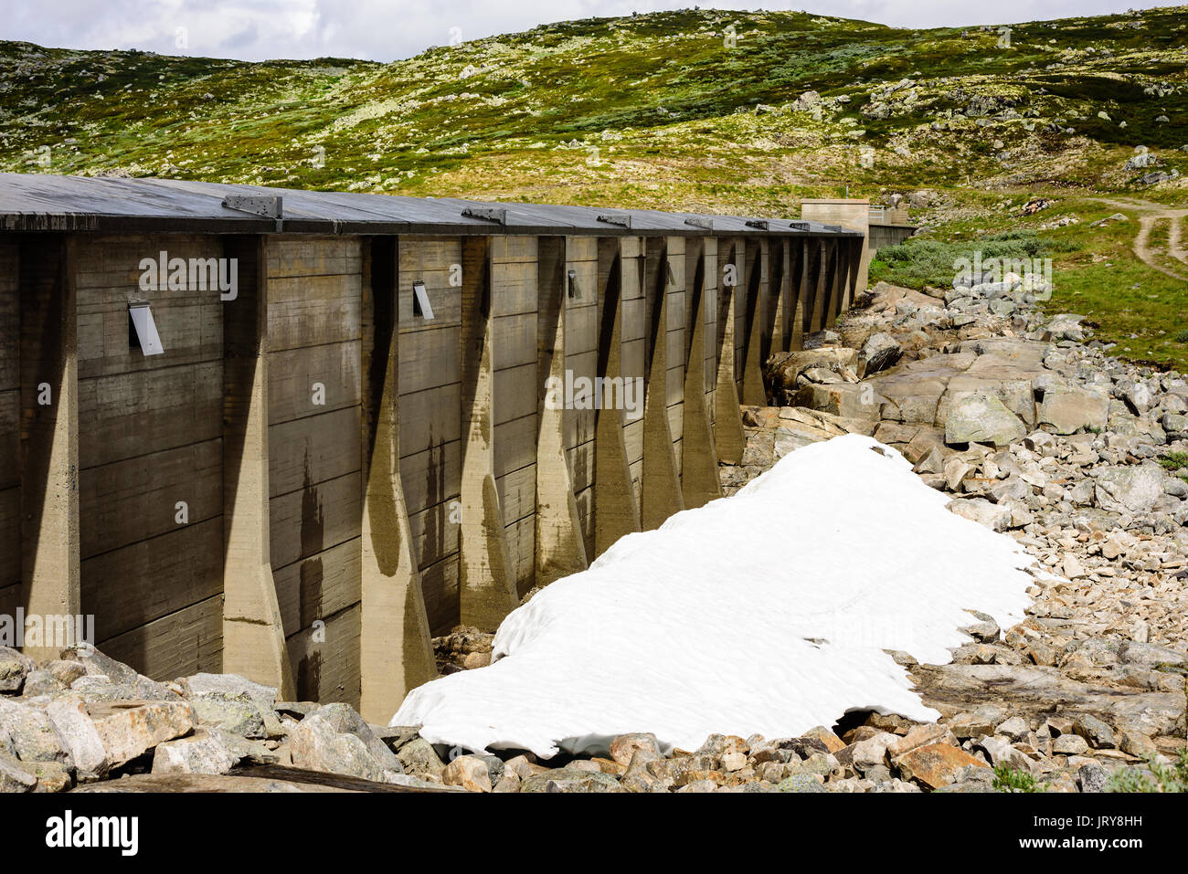 Kleine Haufen Schnee unter Beton Wand oder Damm am Wasserbehälter in Highland Landschaft. Stockfoto